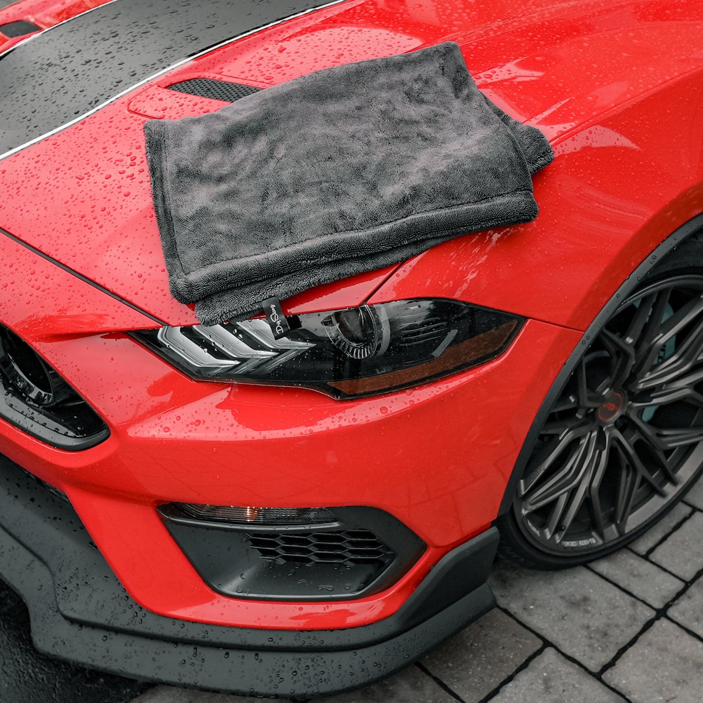 Red car with a black towel on the hood on a wet pavement