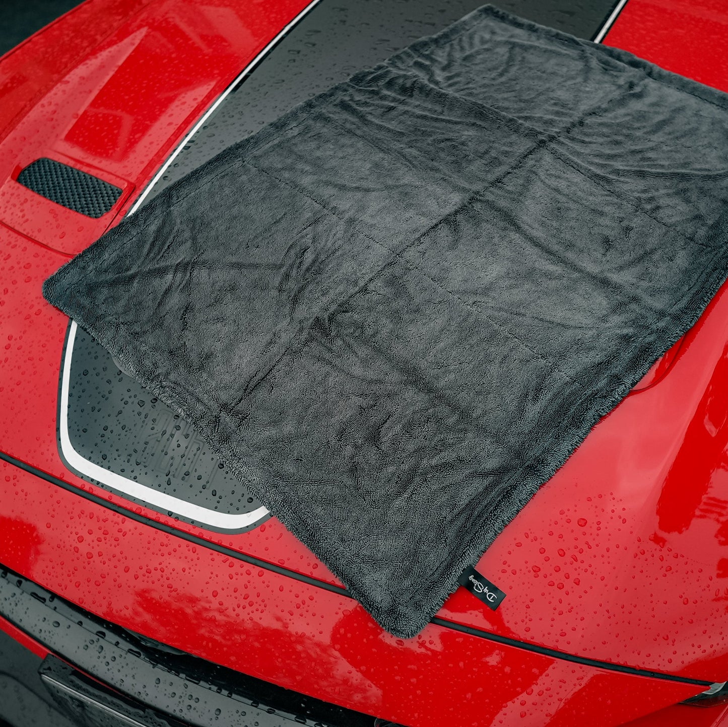 Black car drying microfiber towel draped over a red car