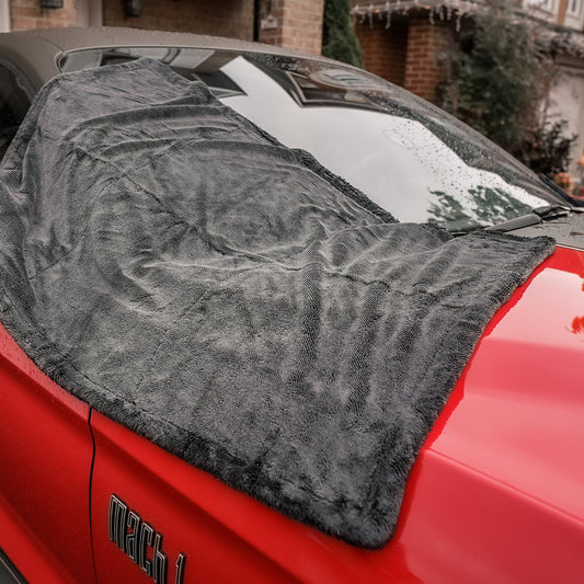 Red car with a gray car drying microfiber towel draped over the windshield in a driveway.