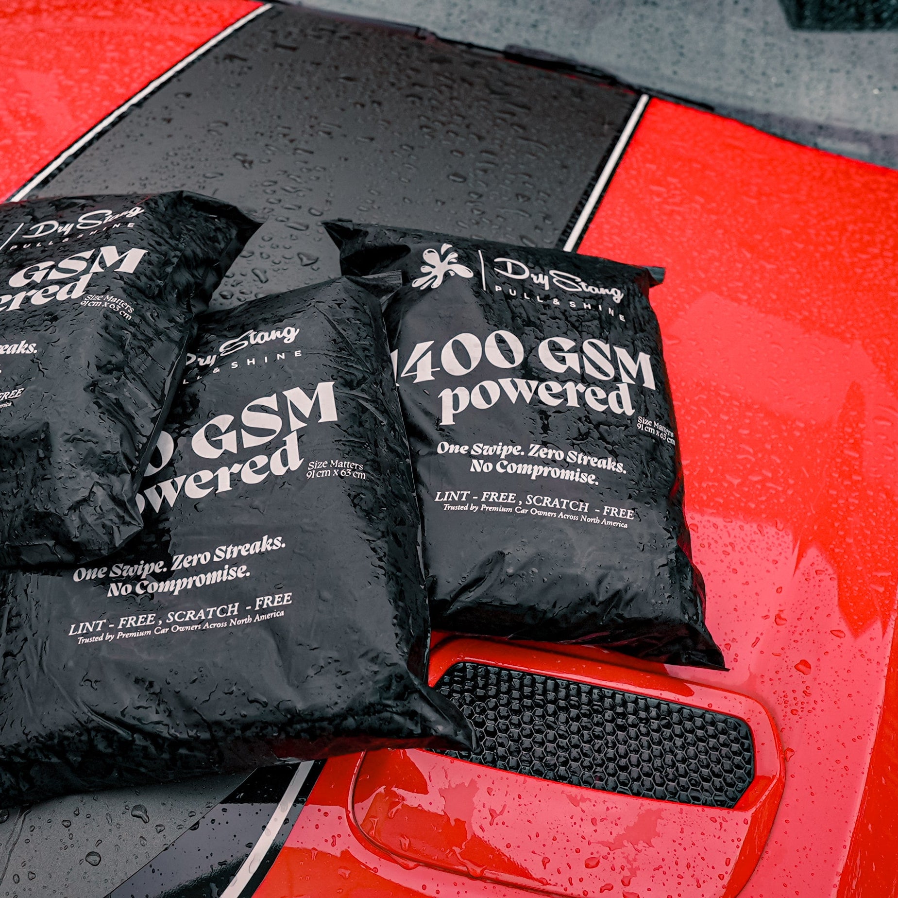 Three black bags labeled '1400 GSM powered' on a red car surface.