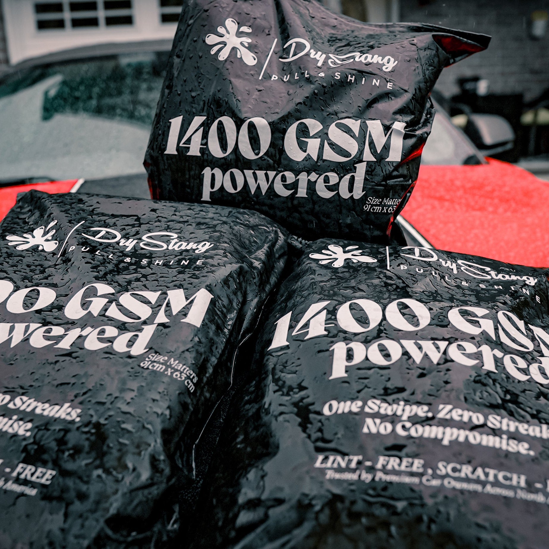 Three black bags labeled '1400 GSM powered' on a red car hood.
